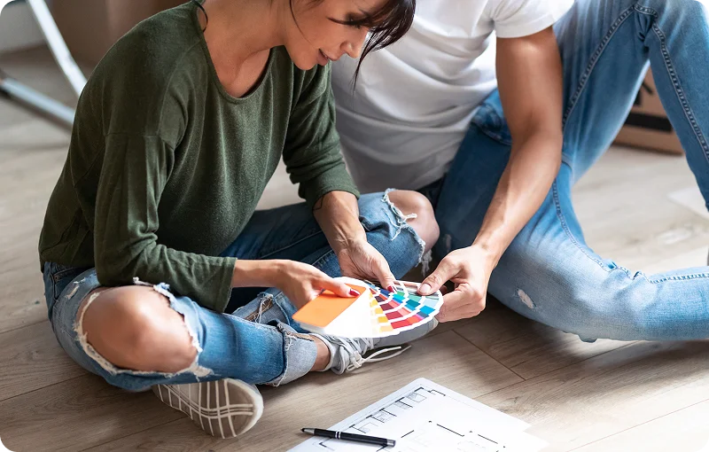 @lang('Casal sentado no chão a escolher cores e materiais para a nova casa, num momento de planeamento facilitado pelo crédito habitação construção.')